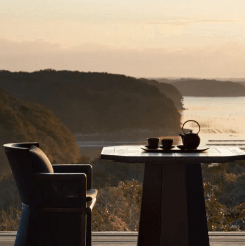 Vista de um ryokan de luxo ao entardecer, com mesa de chá voltada para a baía