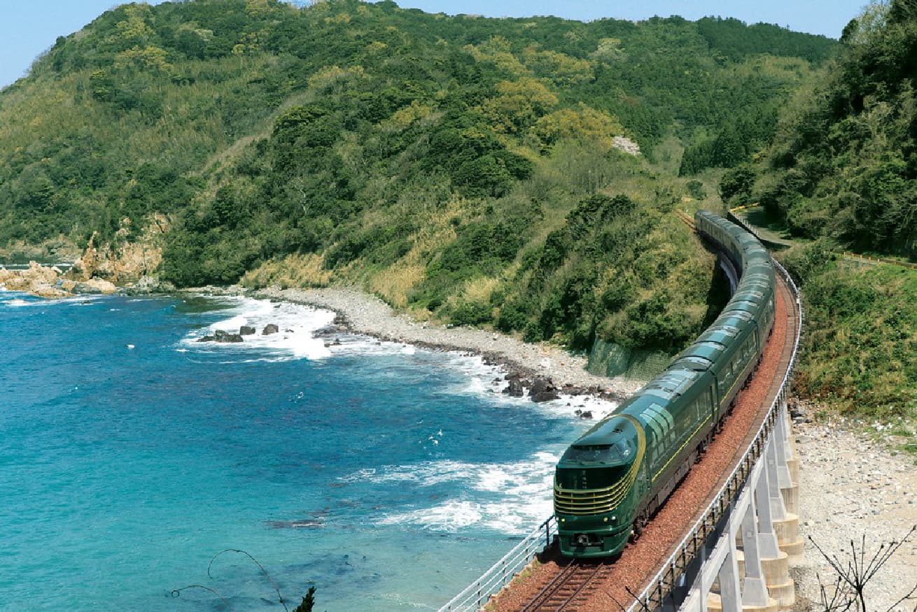 Trem de luxo japonês percorrendo a costa entre o mar e as montanhas